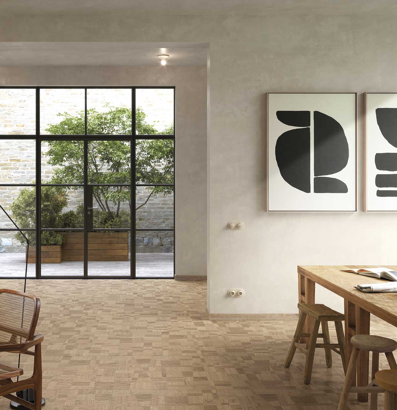 Modern setting with wood-effect woven floor, light rough wood table and stools, abstract paintings, and window to courtyard.