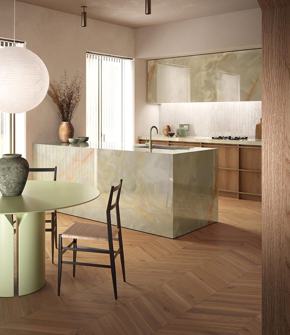 Cucina contemporanea con isola rivestita in Gemme Onice Miele Brillante, pavimento in legno e arredi dalle linee essenziali.