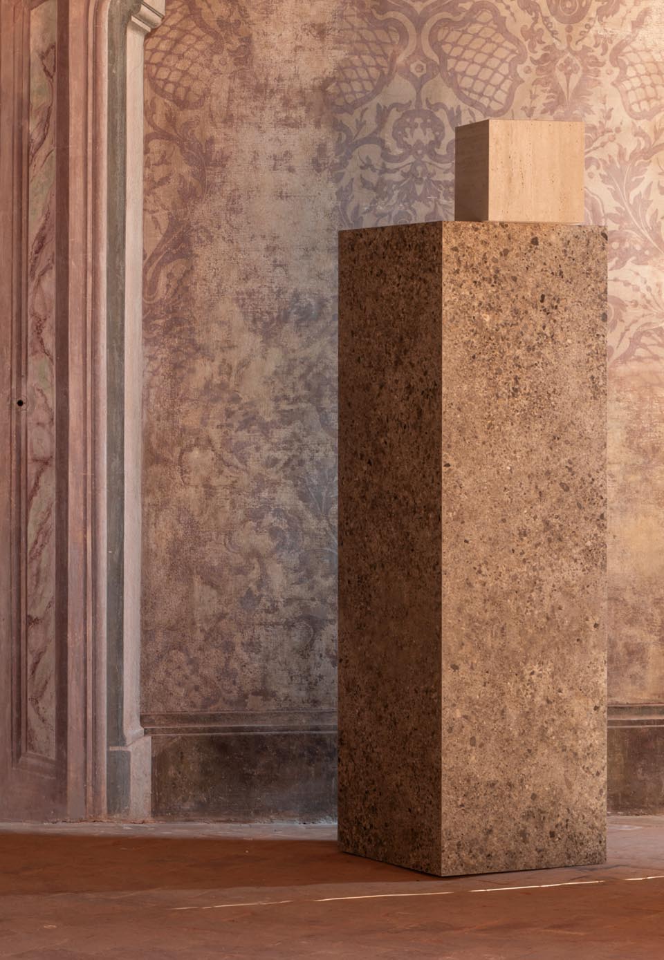 Stone-effect ceramic columns with a porous texture and brown hues, set against classic frescoed walls.