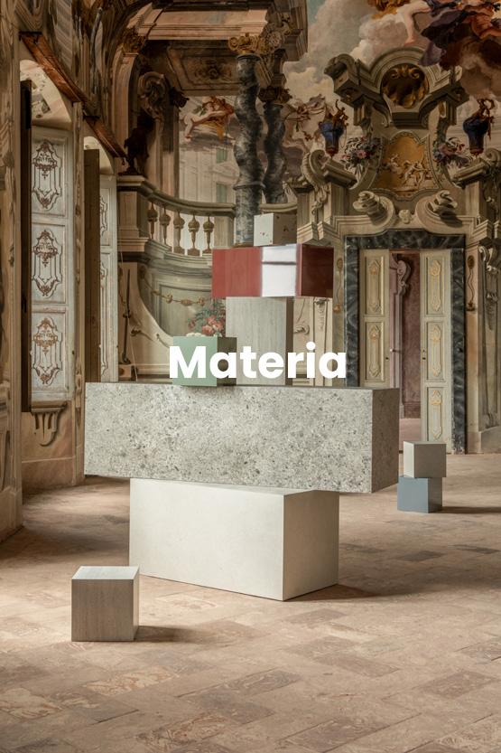 Artistic installation of stone-effect ceramic blocks and colored surfaces, set in a baroque-style frescoed room.