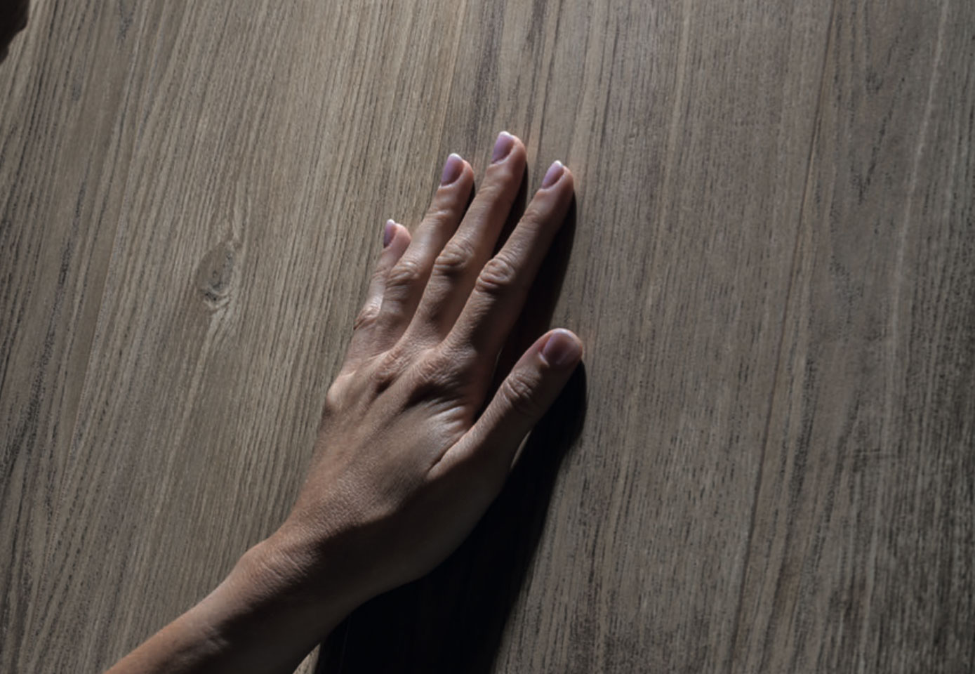 Hand caressing natural wood-effect surface with realistic grain and warm medium oak tone finish.