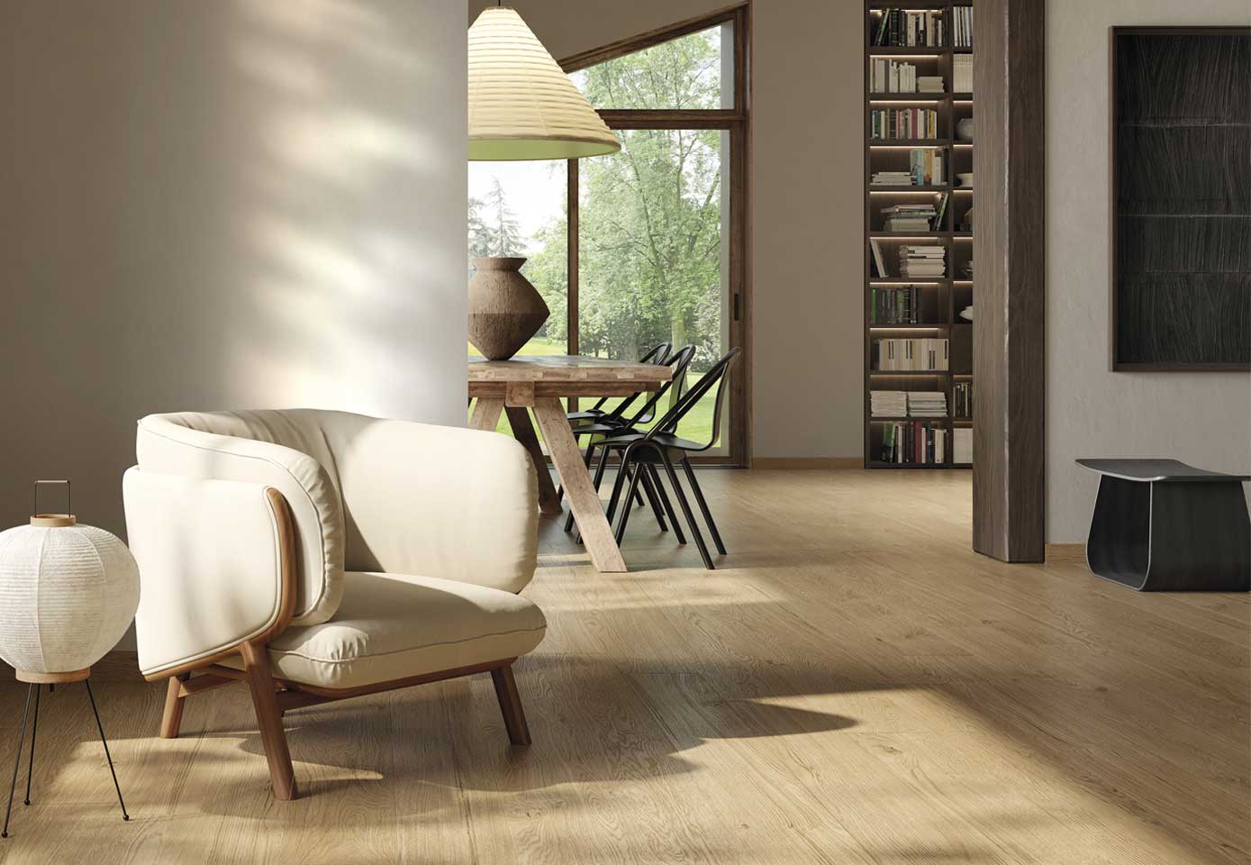 Modern living room with light wood-effect stoneware floor, minimal wood furniture and cream upholstered armchair, built-in bookcase, large window overlooking garden.
