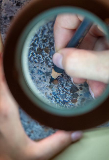 Detail of artisan workmanship with pencil and magnifying glass on stone-effect surface.