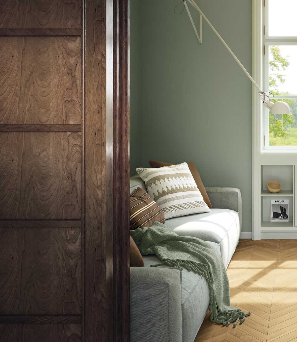 Living room with light wood effect floor in plug, sage green walls, gray sofa, decorative pillows, window to courtyard.