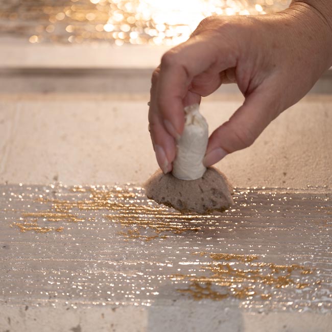 Manual application of gold decorations on a glossy tile, relief work and luminous reflections.