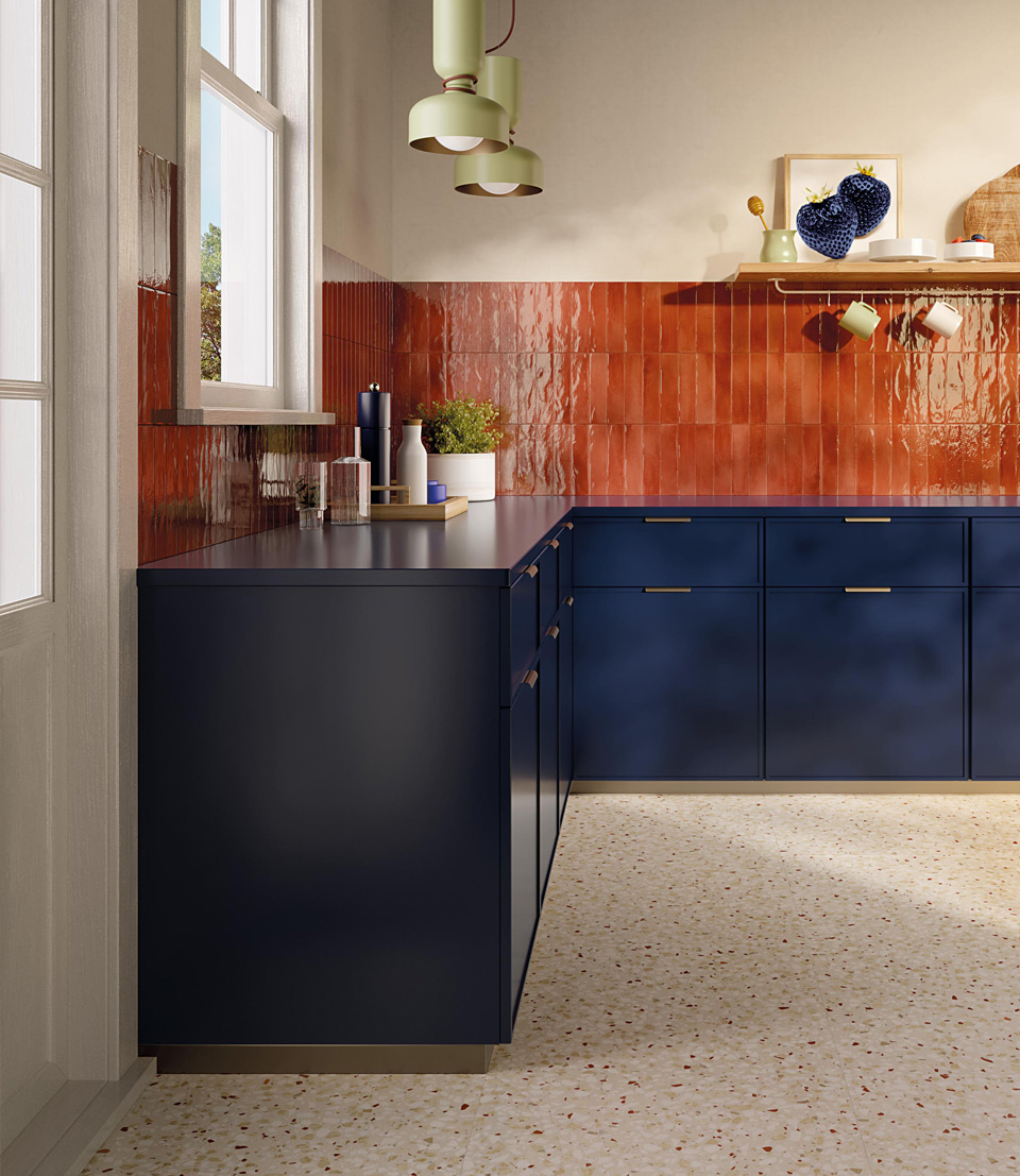 Cucina moderna con basi blu opaco, rivestimento lucido rosso terracotta, top nero e pavimento terrazzo beige con graniglia colorata.