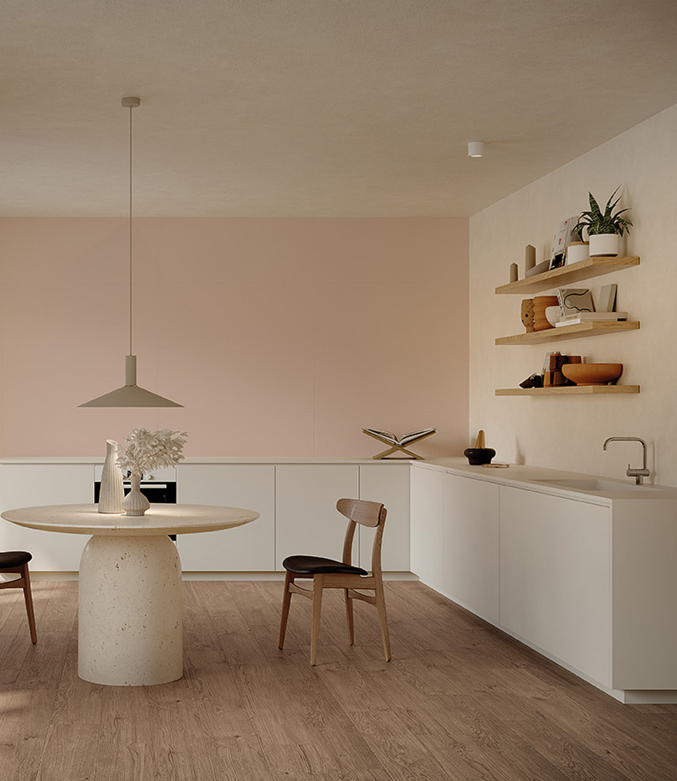 Cucina moderna minimal con mobili bianchi opachi, pavimento effetto legno, parete rosa cipria e tavolo rotondo in pietra naturale.
