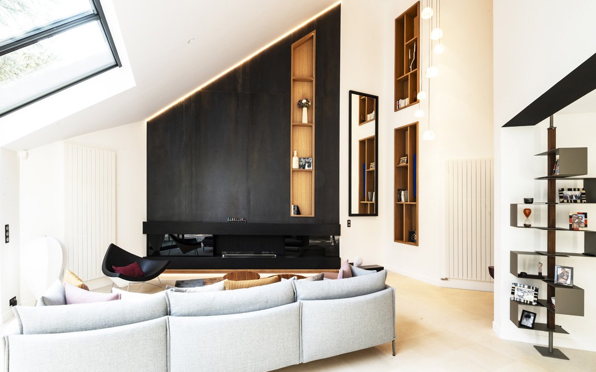 Salón contemporáneo con paredes blancas y paneles oscuros, sofá gris y detalles luminosos para un diseño elegante y minimalista.